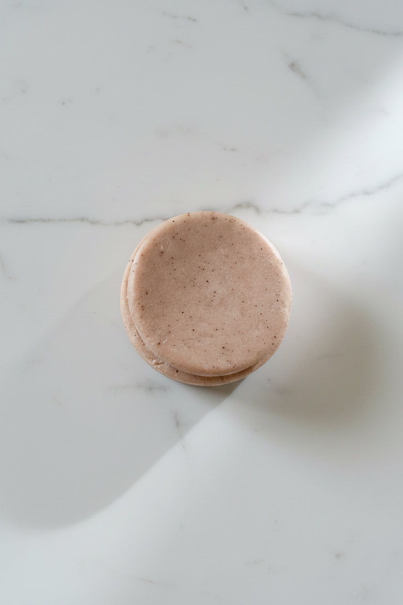Round pink shampoo bar on a light gray surface