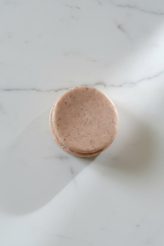 Round pink shampoo bar on a light gray surface