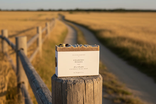 Bar of soap labeled "Country Roads," set upon a wooden fence post, with sprawling country road in the background.
